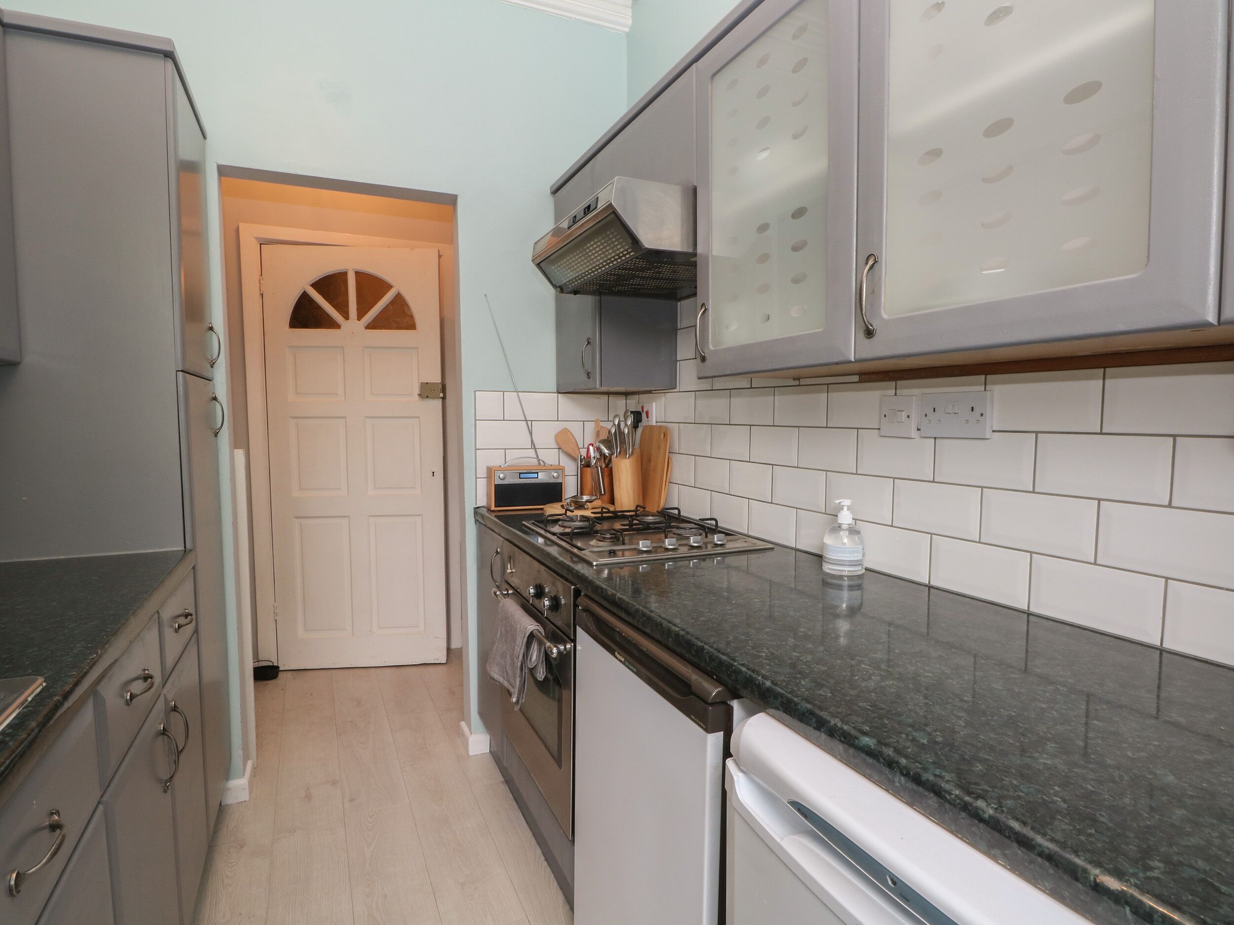 Cocina con estufa, horno y lavavajillas. Hay una puerta que da a otra habitación.