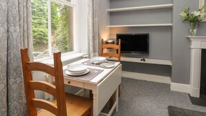 A dining area with a table set for two, a television mounted on the wall, and a fireplace. - Belvedere (Buxton)