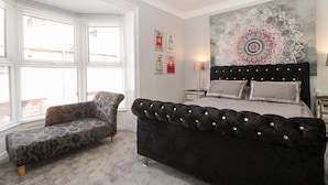 Een slaapkamer met een groot bed, een stoel, een wandtapijt en een raam met jaloezieën.