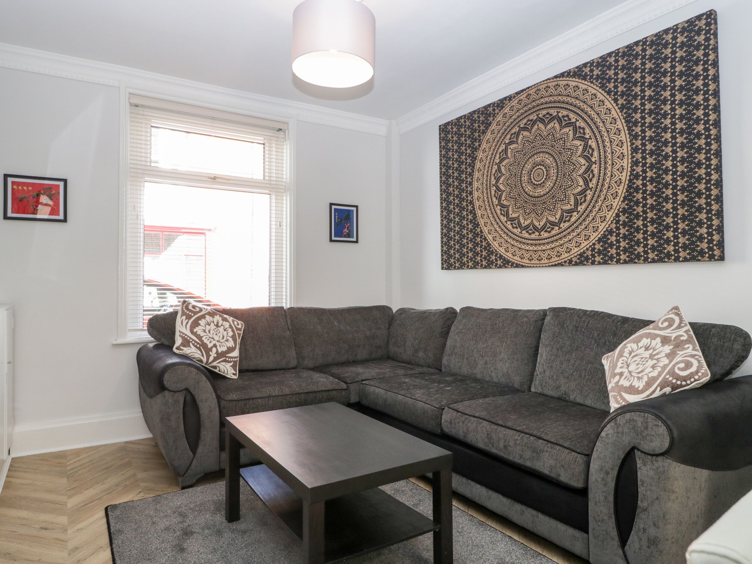 A modern living room with a sectional sofa, a coffee table, and a large tapestry on the wall.