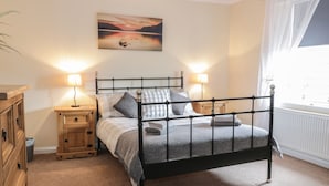 A bedroom with a metal bed frame, two bedside tables with lamps, a wooden dresser, and a painting on the wall. - The Antlers (Coldstream)