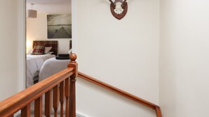 A staircase with wooden railings leading to a bedroom with a bed, a nightstand, and a painting on the wall. - The Antlers (Coldstream)