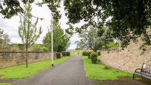 A paved pathway flanked by stone walls and greenery, leading to a distant building. - The Antlers (Coldstream)