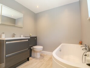A modern bathroom with a large bathtub, a toilet, and a vanity with a mirror. - Trevore Farmhouse (Truro)