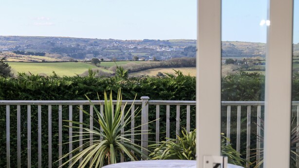 A balcony with a view of a rural landscape, a round table, and a potted plant. - Trevore Farmhouse (Truro)