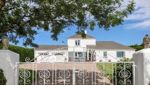 A gated entrance to a white house with a brick pathway leading to the front door. - Trevore Farmhouse (Truro)