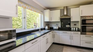 A modern kitchen with white cabinets, a black countertop, a stainless steel range hood, and a built-in oven. - Trevore Farmhouse (Truro)