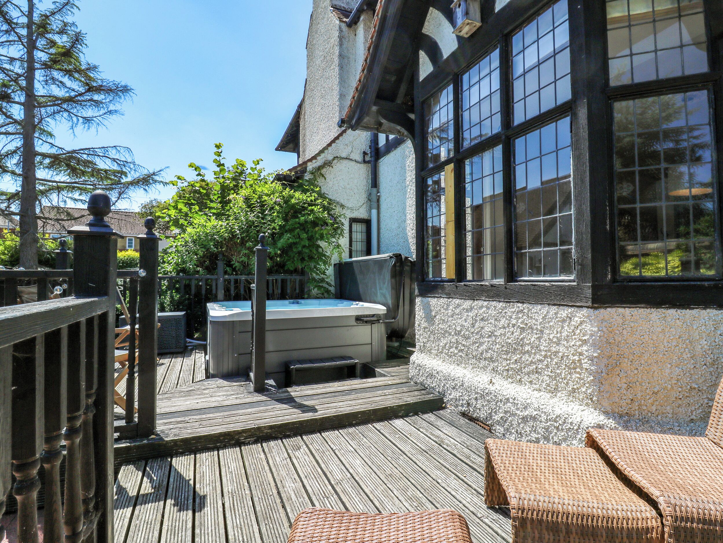 A wooden deck with a hot tub, a fenced garden, and a building with large windows.
