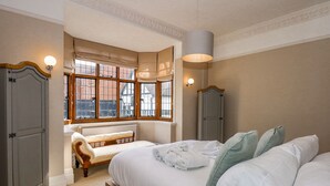 Un dormitorio con una cama grande, una ventana con cortinas, un armario y un banco.