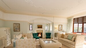 Amplia sala de estar con chimenea, sofás de estampado floral y un sillón verde.