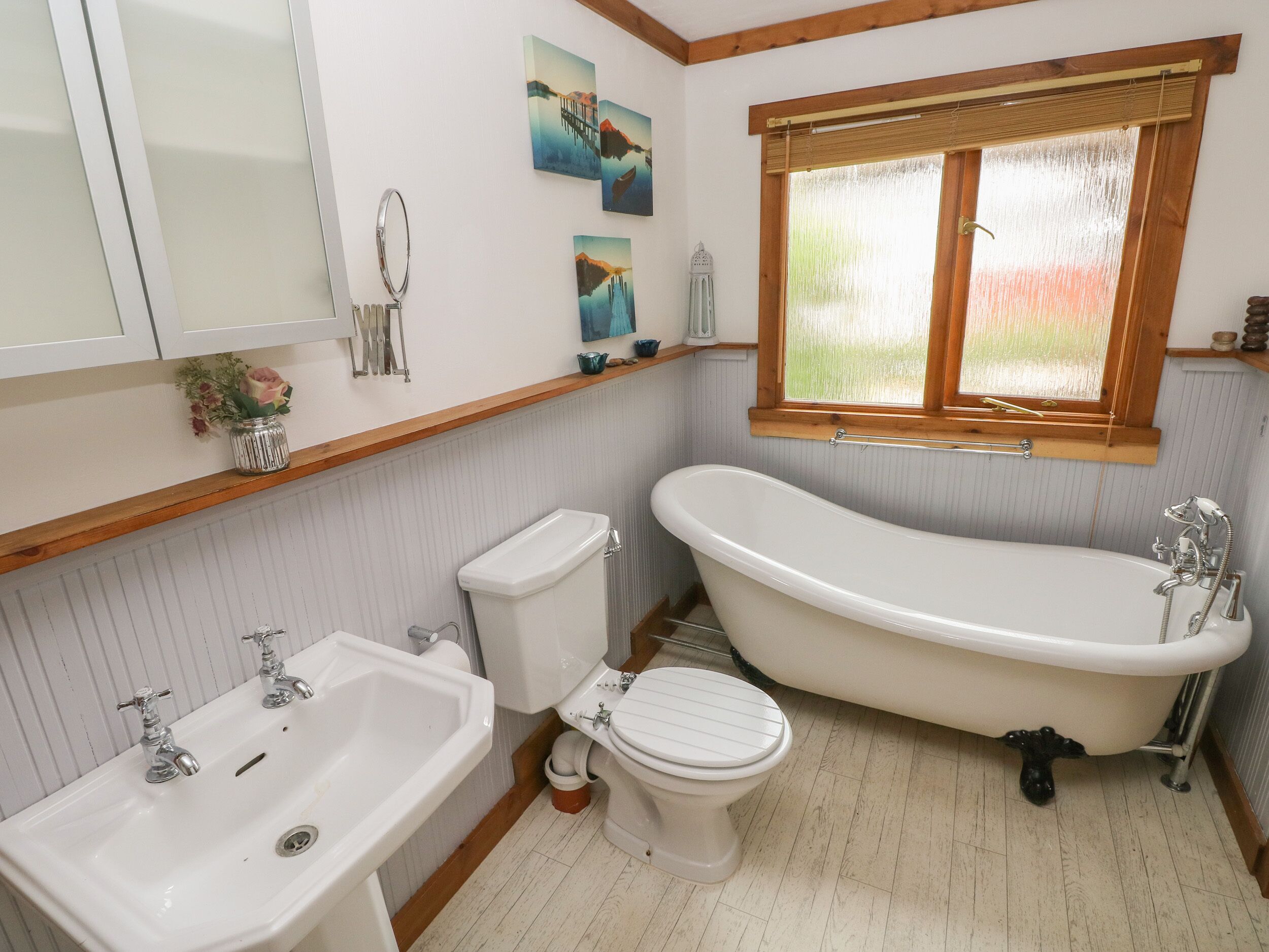 A bathroom with a freestanding bathtub, a sink, a toilet, and a window with a wooden frame.