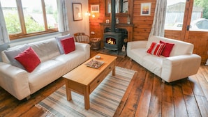 Ein gemütliches Blockhauszimmer mit zwei weißen Sofas, einem Holztisch, einem Kamin und großen Fenstern.