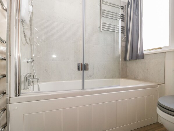 A modern bathroom with a glass-enclosed shower, a white bathtub, and a toilet.