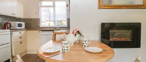 A kitchen with wooden cabinets, a microwave, a sink, and a window with curtains. There is a dining table with chairs and a vase of flowers.