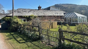 A rustic cottage with a brick exterior, a wooden fence, and a greenhouse. - Stable Cottage (Taunton)