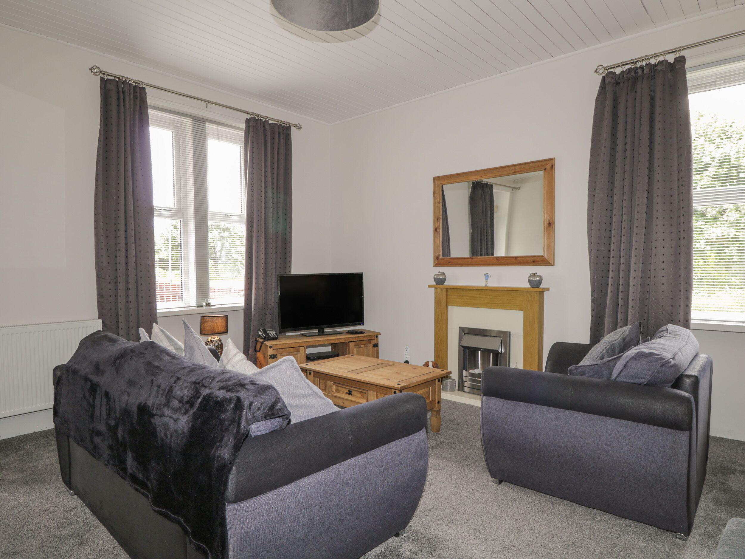 A living room with two sofas, a TV, a fireplace, and large windows with curtains.