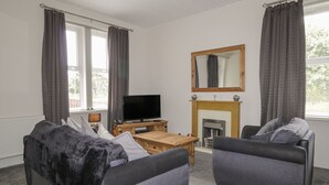 Ein Wohnzimmer mit zwei Sofas, einem Fernseher, einem Kamin und großen Fenstern mit Vorhängen.
