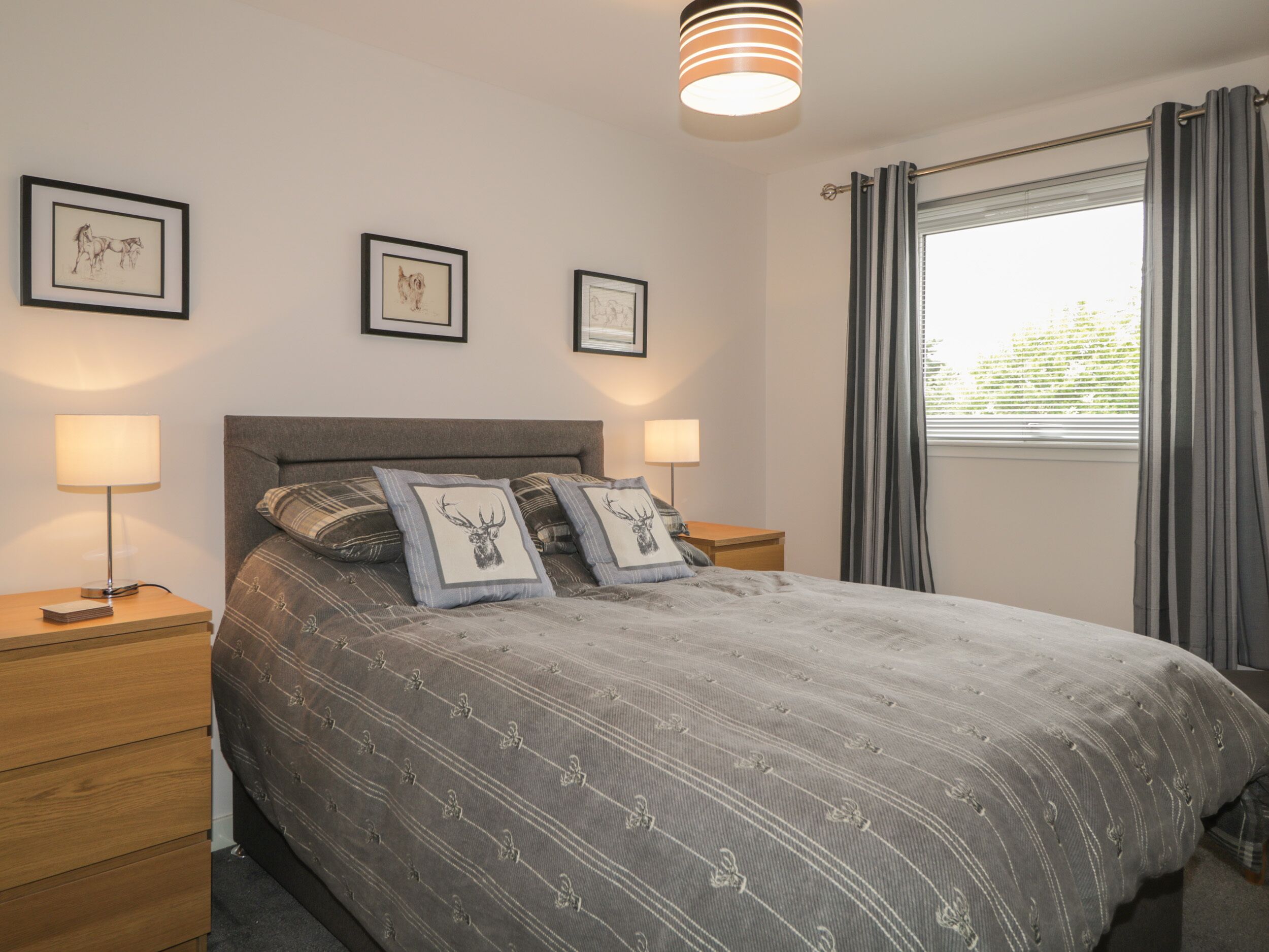 Une chambre à coucher avec un lit, deux tables de chevet, une lampe et des tableaux encadrés accrochés au mur.
