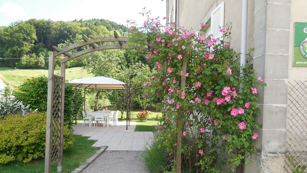 A garden pathway leading to a covered outdoor seating area with a pergola and a table set for dining. - Charming 5-Bedroom House with Large Garden, Terrace, and Authentic Decor in Le Val-d'Ajol (Le Val-d'Ajol)