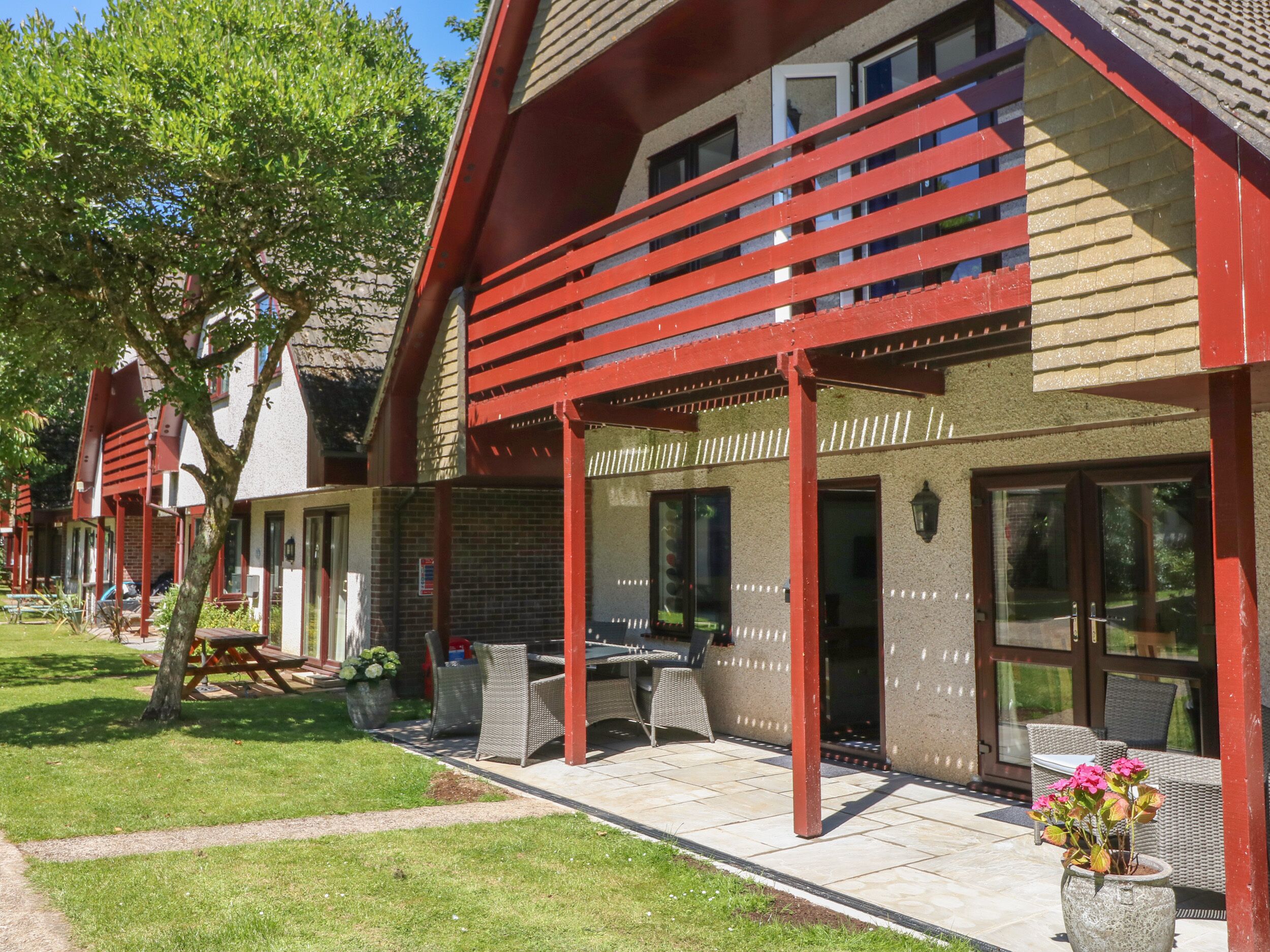 A row of modern houses with red accents, outdoor seating, and a well-maintained lawn.