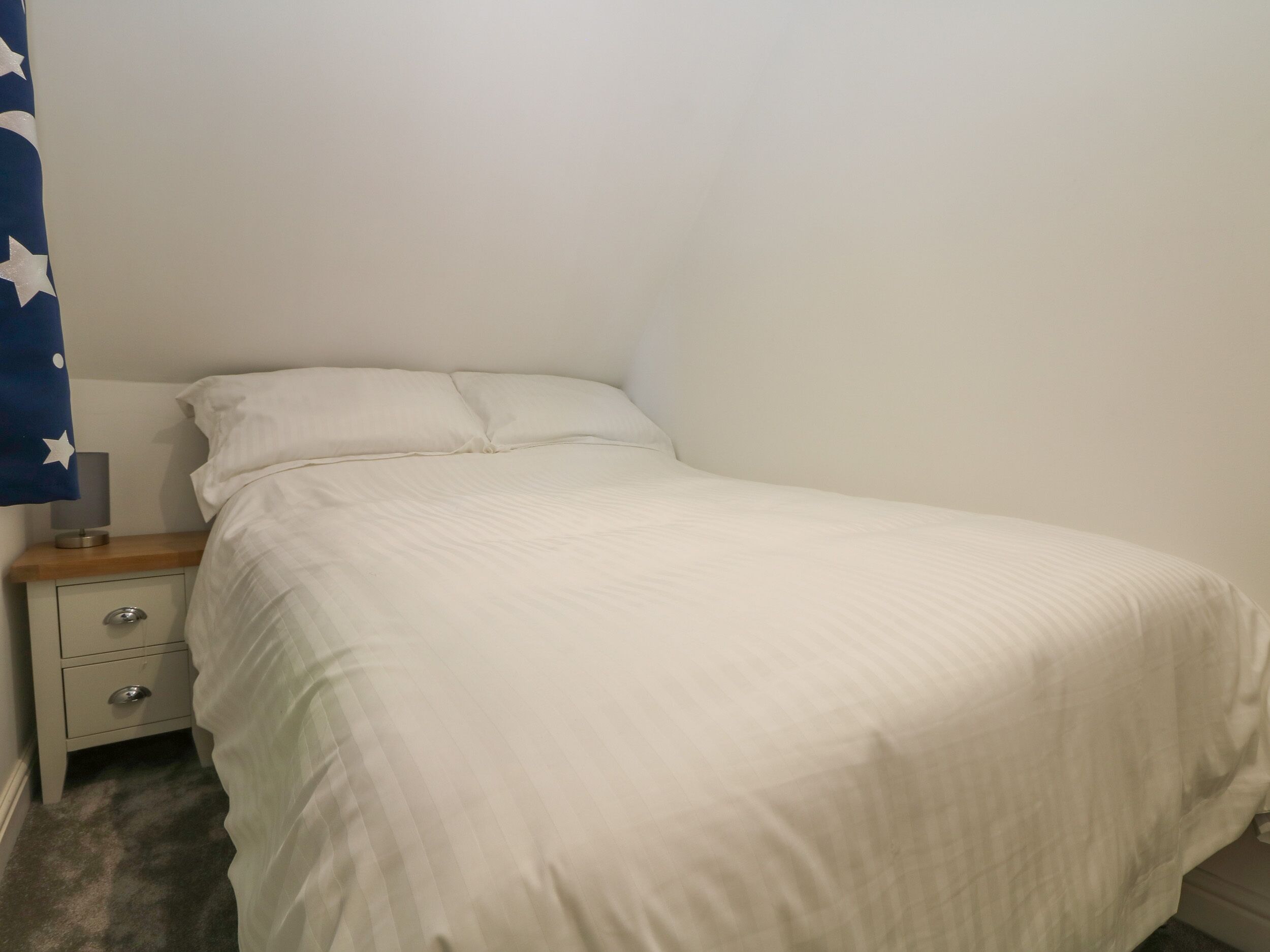 A small, neatly made bed with white bedding in a minimalistic room.