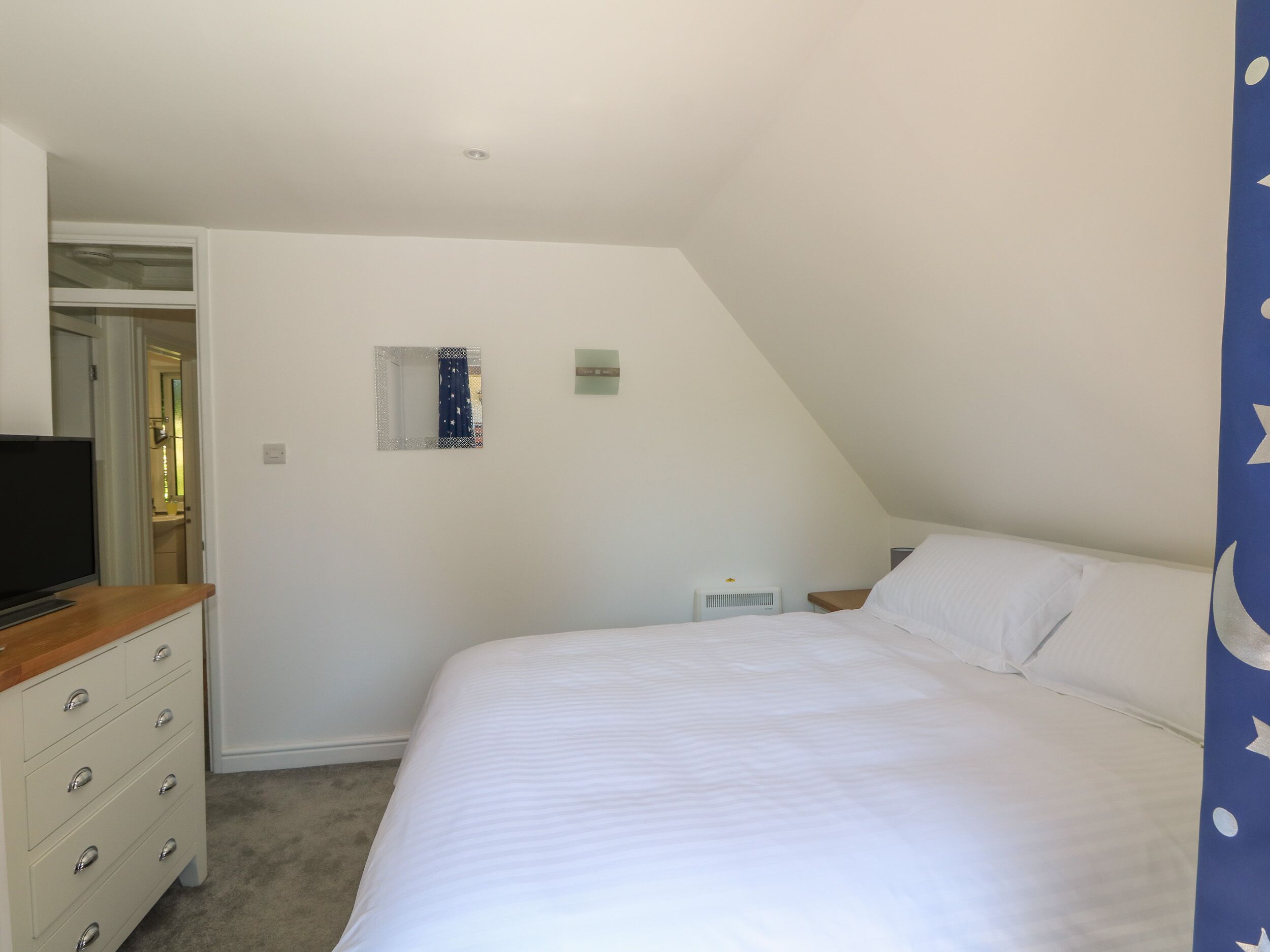 Ein Schlafzimmer mit Bett, Kommode, Fernseher, Spiegel und Fenster.