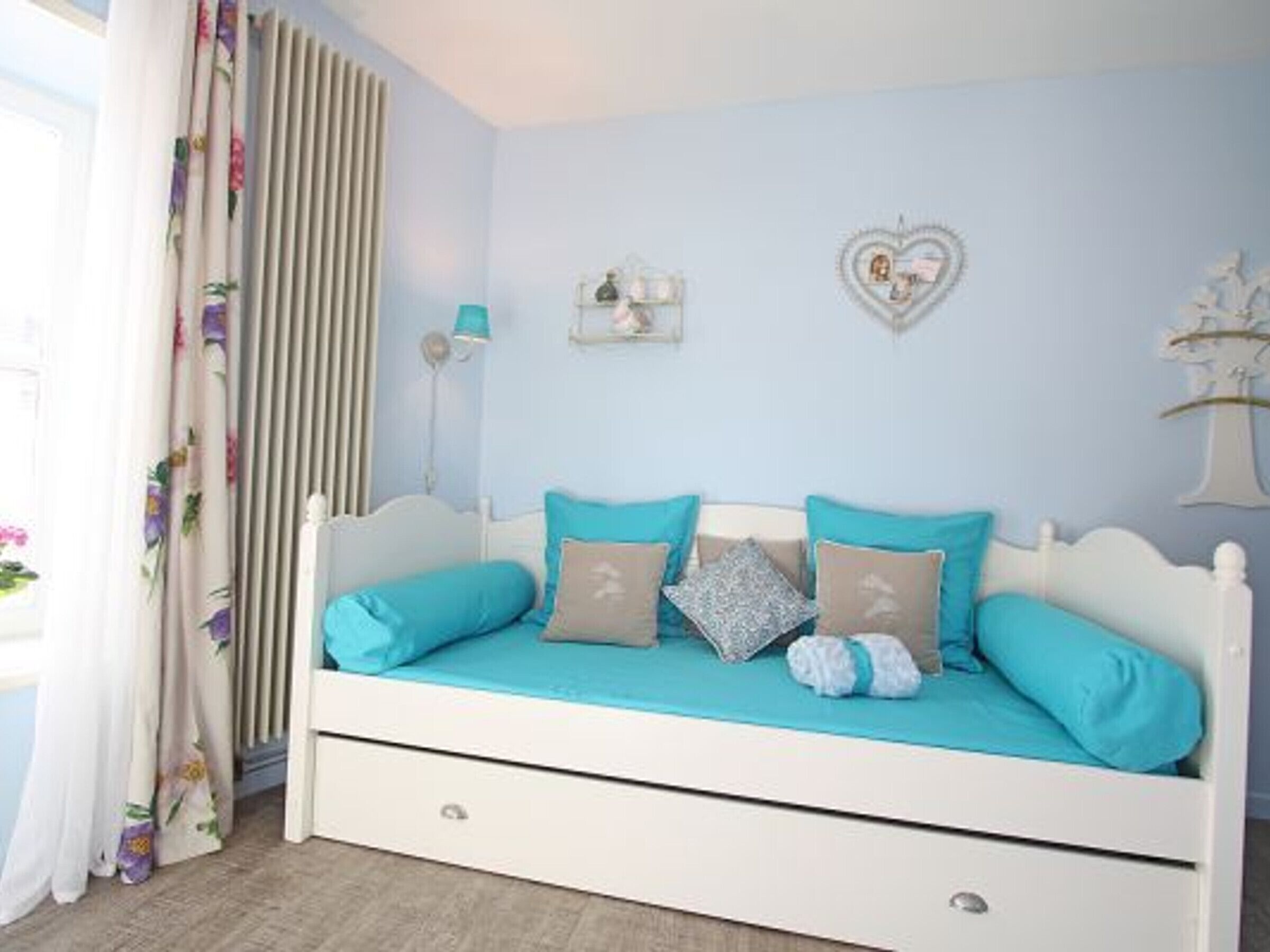 A bedroom with a white bed, teal bedding, and a floral curtain.