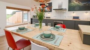Une cuisine moderne avec une table à manger en bois pour quatre personnes, une grande fenêtre et un luminaire suspendu contemporain.