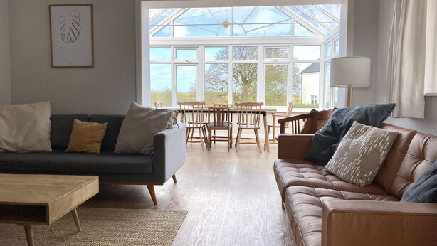 A spacious living room with a large glass door leading to an outdoor area, a wooden dining table, and two sofas. - Auverne (Bude)