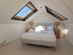 A bedroom with a bed, two bedside tables, a radiator, and skylights. - Auverne (Bude)