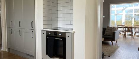 A compact kitchen with a built-in oven and a small stovetop, adjacent to a dining area with a view through large windows.