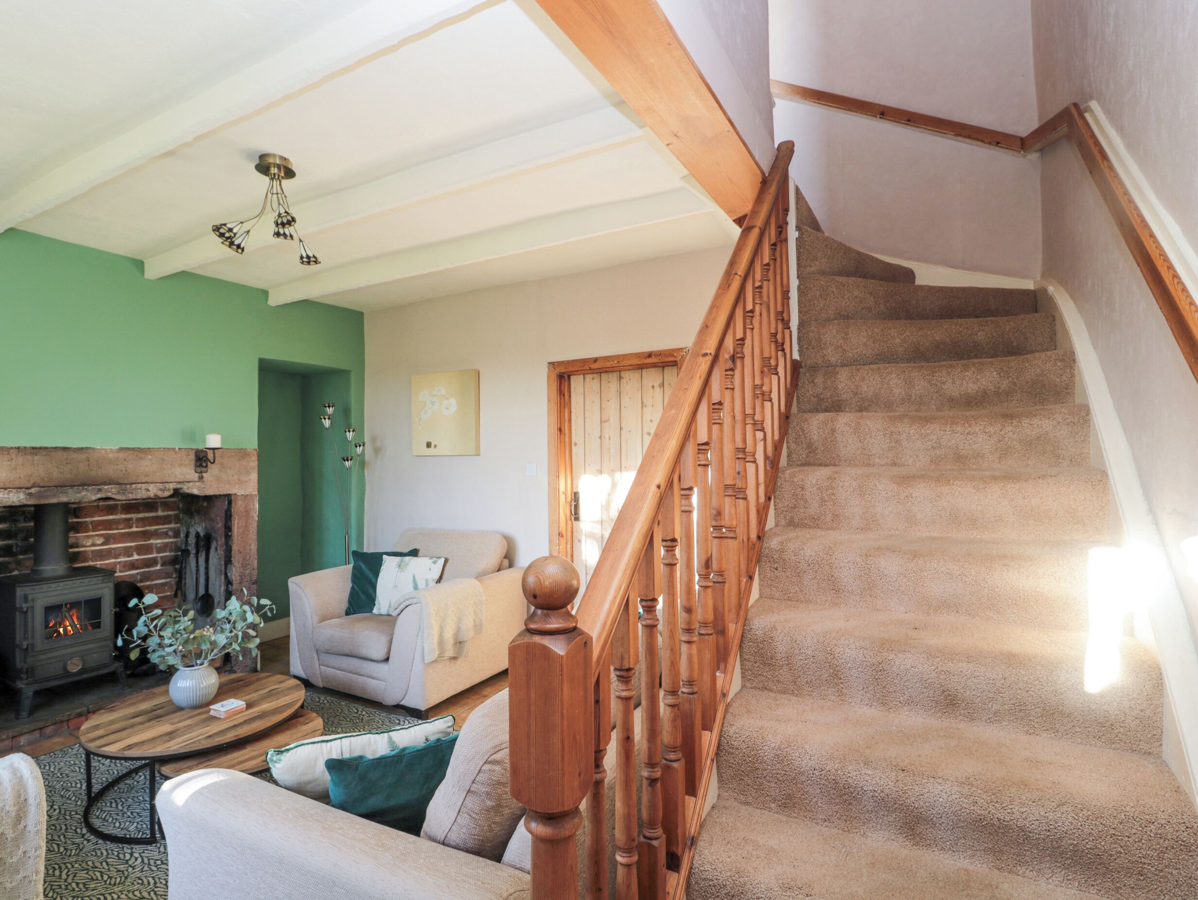 Uma sala de estar aconchegante com lareira, escada e parede verde.
