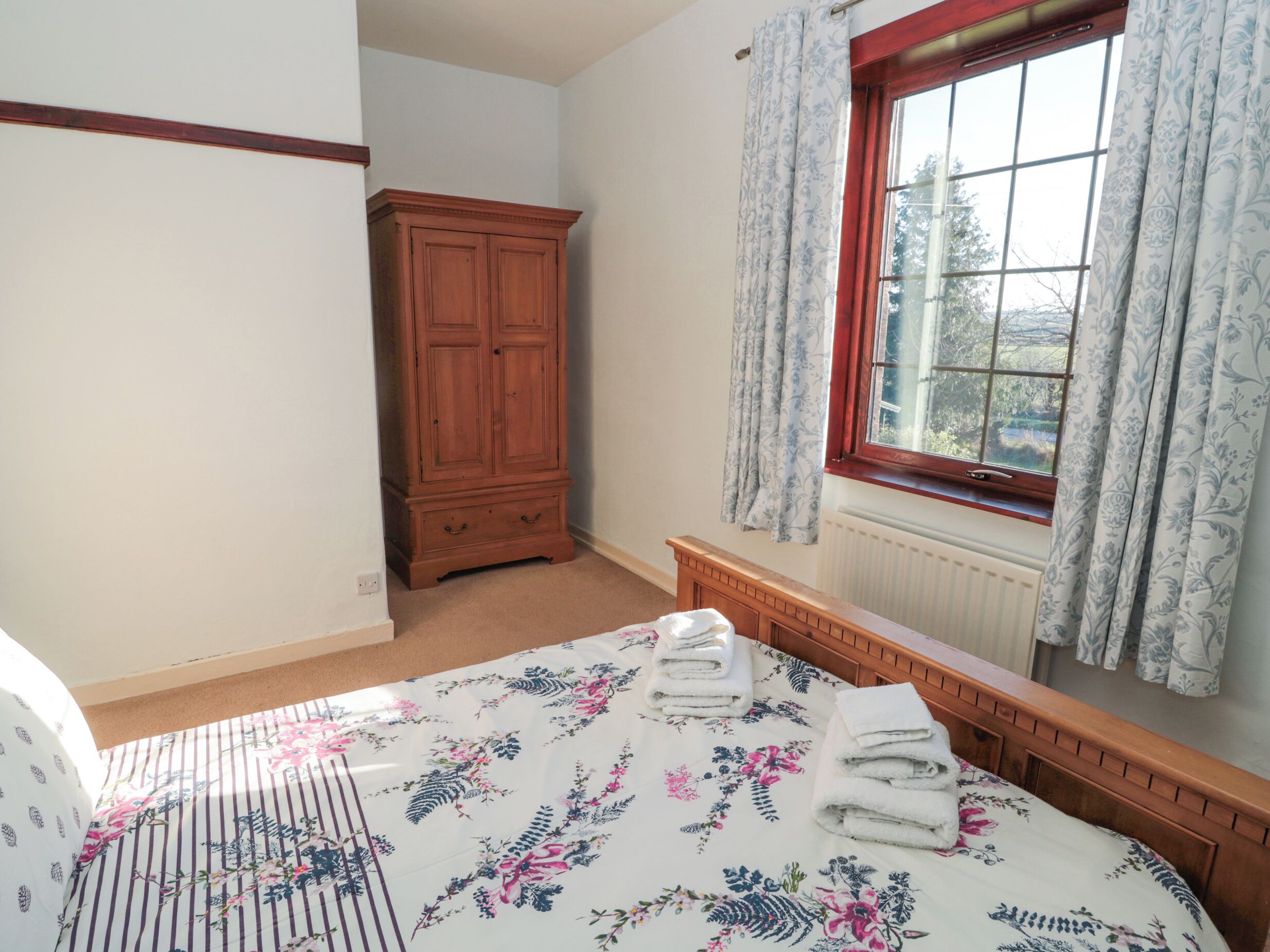 Un dormitorio con cama, armario de madera, ventana con cortinas y radiador.