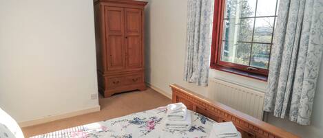 Un dormitorio con cama, armario de madera, ventana con cortinas y radiador.
