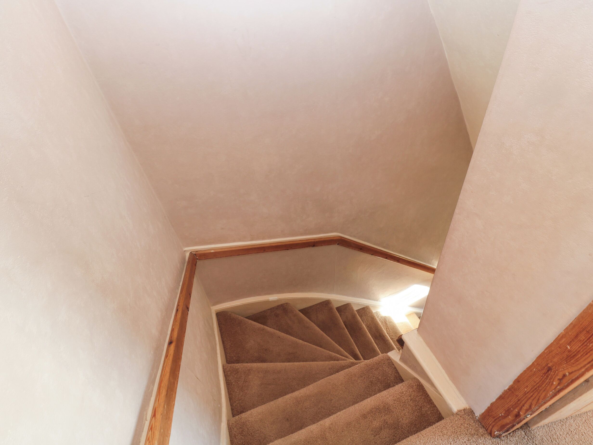 A spiral staircase with carpeted steps and wooden handrails, leading to an upper floor.
