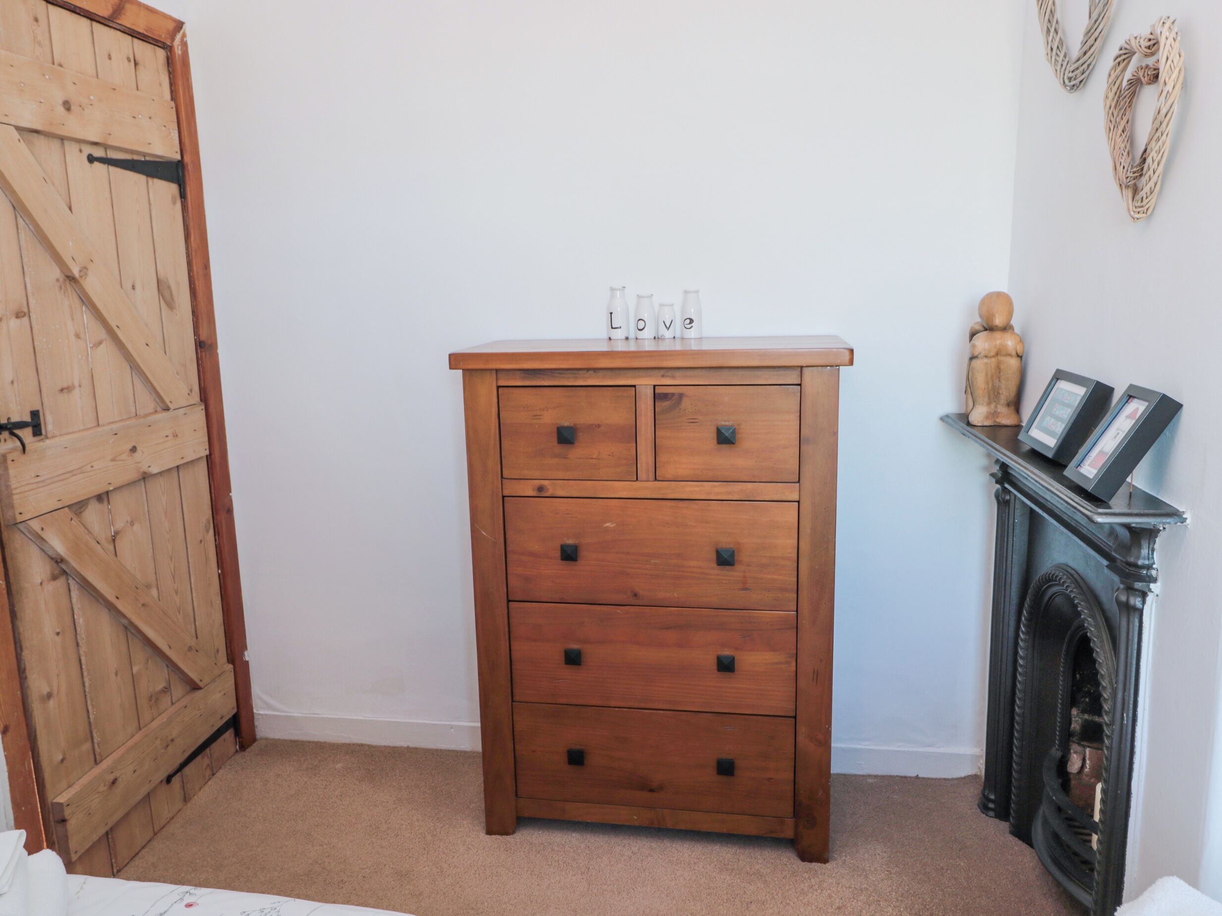 A wooden dresser with drawers, a small shelf with decorative items, and a fireplace.