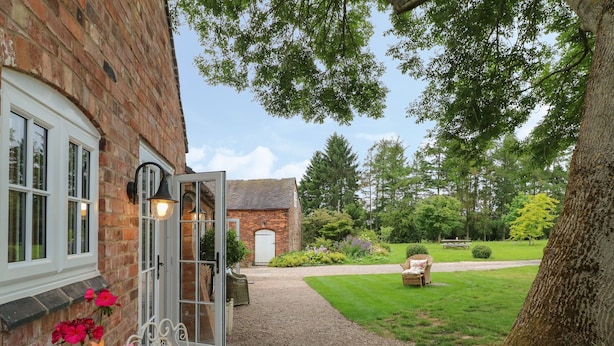 Um edifício de tijolos com um caminho de brita que leva a um jardim, onde há uma cadeira de vime e uma mesa.