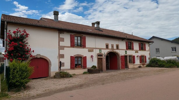 En toetages bygning med røde døre og vinduer, et tagtækket tag og en grusbelagt indkørsel.