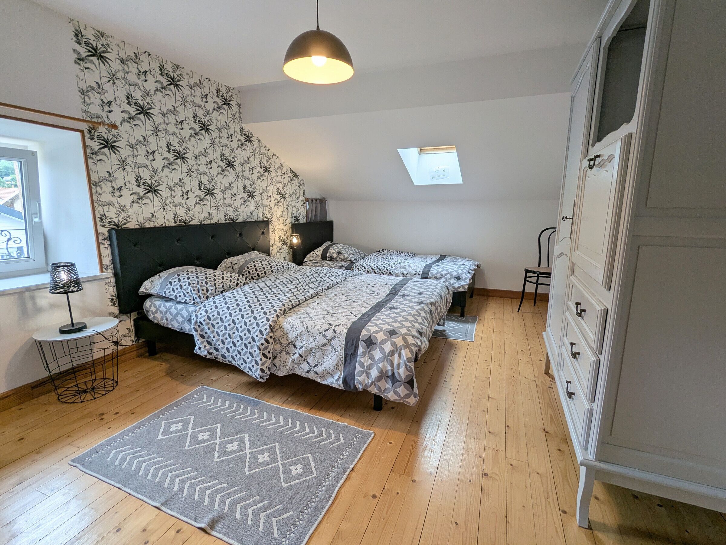 Une chambre avec deux lits, une commode, une fenêtre et un mur décoré de motifs.