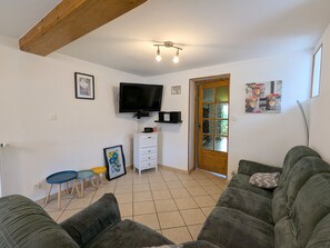 Una sala de estar con televisor, una puerta de madera y suelo de baldosas.