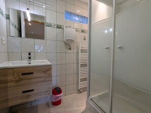 Een badkamer met een witte wastafel, een houten kastje, een glazen douchecabine en een handdoekwarmer.