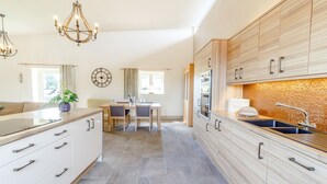 Une cuisine moderne avec des meubles en bois, un coin repas comprenant une table et des chaises, et un lustre.