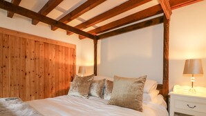 Een slaapkamer met een houten plafond, een bed met witte lakens en twee bedlampjes.