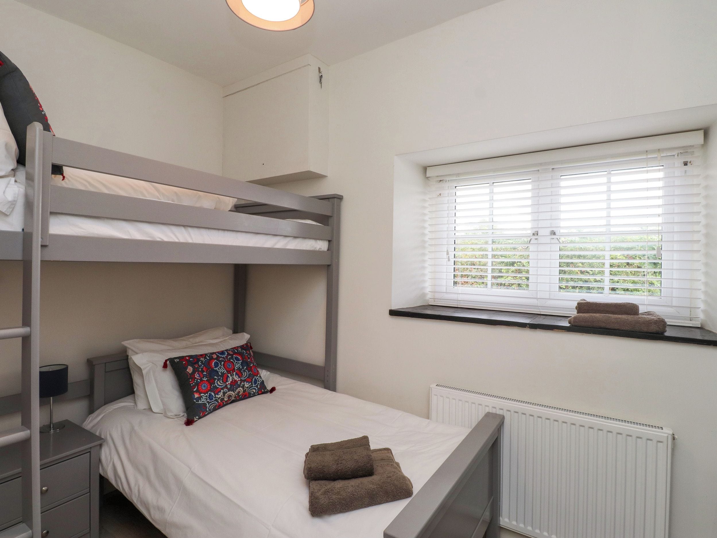 A bunk bed room with a window, a bedside table, and a radiator.