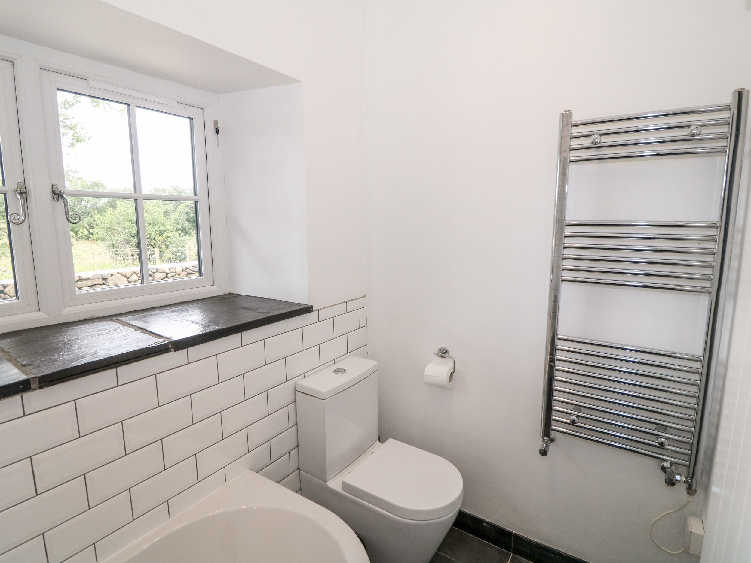 A bathroom with a toilet, a bathtub, a window, and a towel rack.