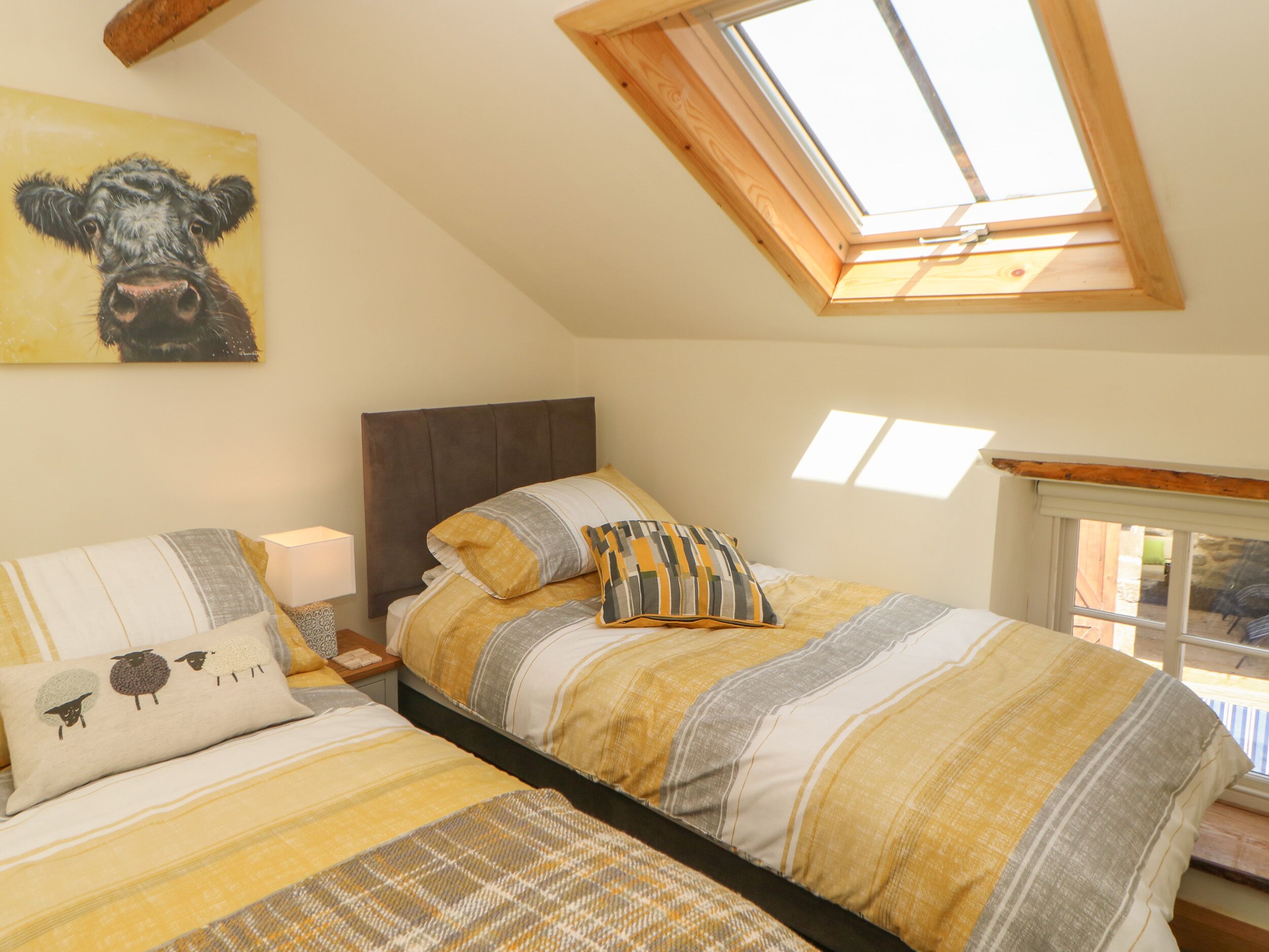 Ein Schlafzimmer mit schrägem Dach, einem Oberlicht, einem Bett mit gestreifter Bettwäsche und einem Bild einer Kuh an der Wand.