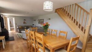 A dining area with a wooden table and chairs, a vase with flowers, and a staircase. - Delfryn (Denbigh)