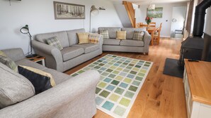 A cozy living room with a grey sofa, a small side table, a floor lamp, and a patterned rug. - Delfryn (Denbigh)