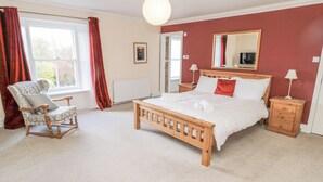 A bedroom with a wooden bed, a chair, a nightstand, a lamp, and a window with curtains. - Jubilee House (Alnwick)