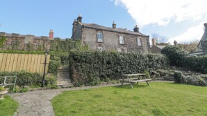 A stone building with a garden, a wooden fence, and a picnic table. - Jubilee House (Alnwick)